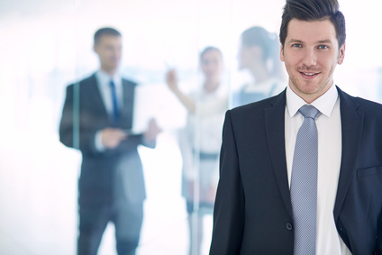 Portrait of young businessman in office with colleagues in the background .